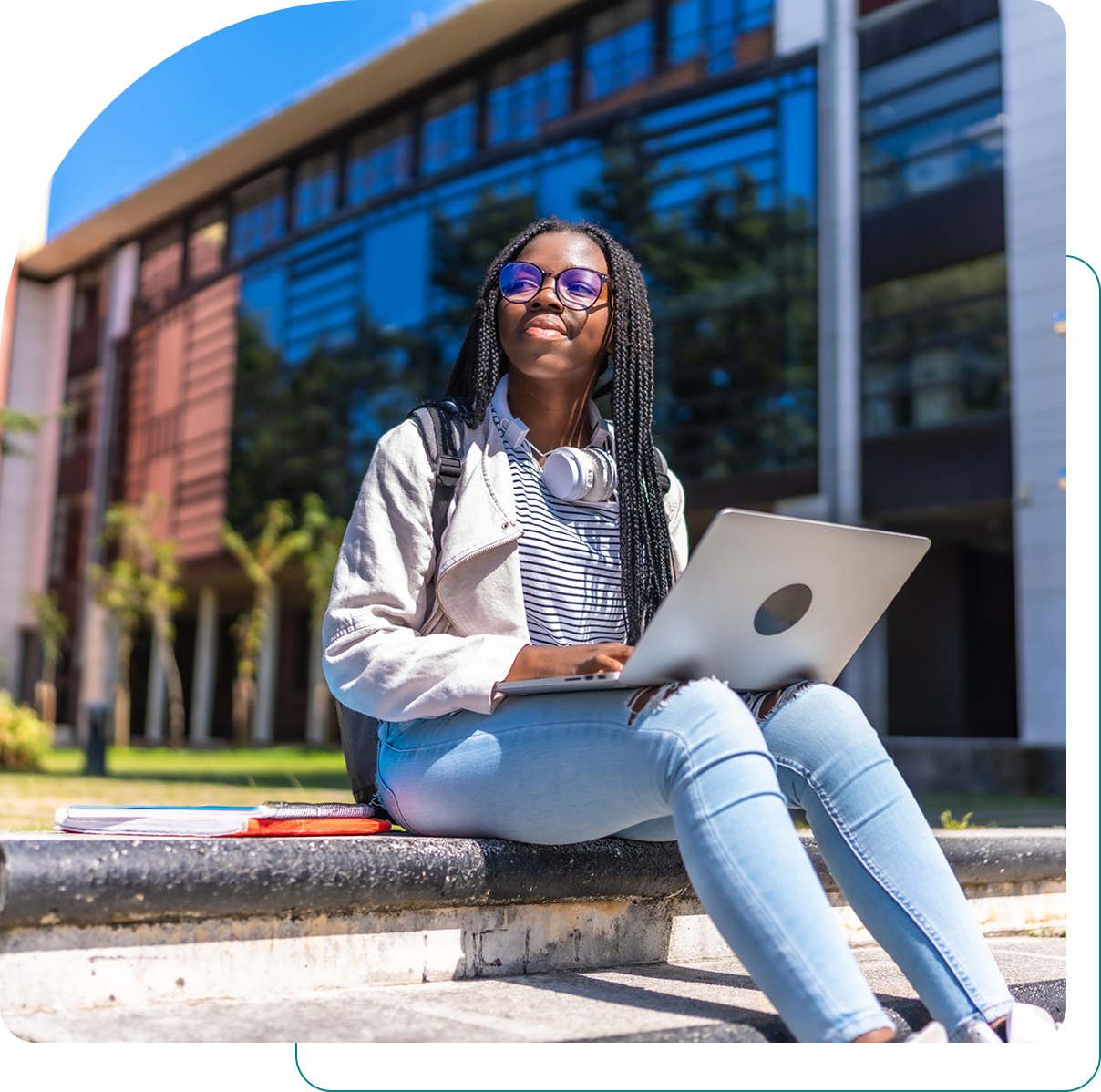 Student with laptop sitting outside modern building.
